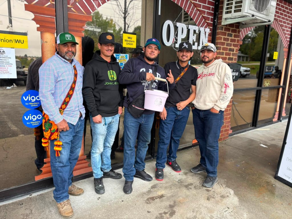 The Carniceria 2 Toros team standing in front of the Danville store, with the OPEN sign and Western Union and Vigo signs in the window.